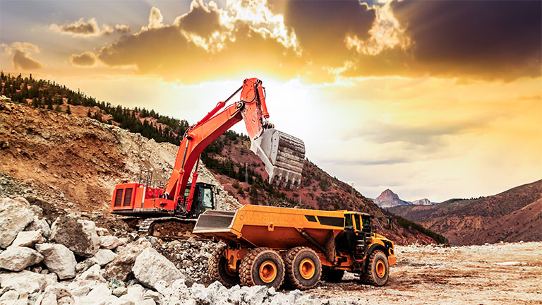 A large excavator dumps a load of rock into a dump truck in an open pit mine.